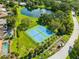 Aerial view of a tennis court and pond with fountain in a lush, green community at 3772 Woodridge Pl, Palm Harbor, FL 34684