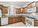 Well-lit kitchen featuring wood cabinets, tile floors, granite countertops, and white appliances at 518 Winthrop Dr, Spring Hill, FL 34609