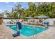 Backyard pool area with lounge chairs, patio umbrellas, lush landscaping, and a basketball hoop at 1242 Whisper Dr, Largo, FL 33770