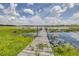 Wooden dock leading to a serene lake with lush greenery and cloudy skies reflecting on the water at 35836 Lakeshore Dr, Dade City, FL 33525