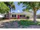Charming single-story home with a pink front door, white exterior, brick accents and beautiful mature trees at 565 55Th Ne Ave, St Petersburg, FL 33703