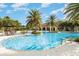 Beautiful resort style pool featuring large palms, tables with umbrellas, a covered pavilion, and blue skies at 5519 Tripoli Dr, Palmetto, FL 34221