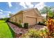 Tan home featuring a two-car garage, brick driveway, manicured landscaping, and decorative outdoor lighting at 644 Chipper Dr, Sun City Center, FL 33573