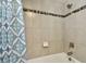 A close up of the bathtub with blue patterned shower curtain and tiled wall with decorative accent at 11002 Sundrift Dr, Tampa, FL 33647