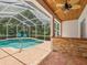 Outdoor kitchen area adjacent to a screened-in pool with a stone bar and ceiling fan at 18803 Misty Shores Ln, Lutz, FL 33548