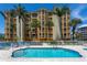 Exterior shot of a building with a pool surrounded by lounge chairs and palm trees at 5353 Gulf Blvd # A402, St Pete Beach, FL 33706