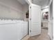 Bright laundry room with white washer and dryer, storage shelves, and a door to another room at 26835 Juniper Bay Dr, Wesley Chapel, FL 33544