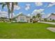 This is an eye-level shot showcasing lush green grass, palm trees, and tasteful landscaping that frame a well-maintained beige house at 602 Deep Lake Ln, Sun City Center, FL 33573