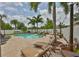 This backyard features a sparkling pool surrounded by palm trees, lounge chairs, and travertine tile at 13728 Artesa Bell Dr, Riverview, FL 33579