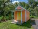 Charming shed with a yellow door and a small porch, nestled in a lush green landscape at 7427 20Th St, Zephyrhills, FL 33540