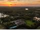 Aerial view of a lush, wooded property with a grand home, tennis court, and a golden sunset backdrop at 18521 Wayne Rd, Odessa, FL 33556