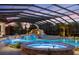 A luxurious covered pool area with a waterfall, slide, and hot tub is softly lit at dusk for romantic evening swims at 18521 Wayne Rd, Odessa, FL 33556