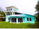 Beautiful turquoise home with floor-to-ceiling glass doors, a charming tower, and a lush green yard at 1626 Sea Breeze Dr, Tarpon Springs, FL 34689