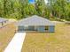 Front view of a inviting blue home with a well-maintained lawn, concrete pathway, and lush green surroundings at 19275 Wildwood Dr, Brooksville, FL 34601