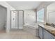 Bright bathroom with tiled floor, separate shower stall and a corner bathtub underneath a large window at 7711 Nottinghill Sky Dr, Apollo Beach, FL 33572