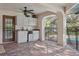 View of the outdoor kitchen area with cabinets, sink, and refrigerator, leading to the pool area through a secure safety fence at 13747 Forest Ridge Ct, Hudson, FL 34667