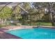 A screened-in pool area featuring brick pavers and views of the surrounding lush landscaping and well-maintained lawn at 13747 Forest Ridge Ct, Hudson, FL 34667