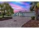 Charming blue home with a paver driveway and lush landscaping under a vivid, colorful sky at twilight at 304 Westwinds Dr, Palm Harbor, FL 34683