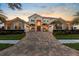 Stunning Mediterranean-style home with lush landscaping, brick driveway, and a beautiful sunset backdrop at 8476 Dunham Station Dr, Tampa, FL 33647