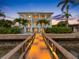 A beautiful three-story waterfront home with balconies and a wooden dock lit up against a twilight sky at 11260 7Th E St, Treasure Island, FL 33706
