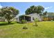 Backyard featuring a screened-in patio, well-maintained lawn, lush landscaping, and mature trees under a blue sky at 4108 Woodtrail Blvd, New Port Richey, FL 34653