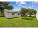 View of backyard and house showing the green grass, mature trees and access to screened in porch area at 4108 Woodtrail Blvd, New Port Richey, FL 34653