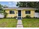 Charming yellow home featuring a lovely front yard with lush green grass, simple landscaping, and a blue front door at 508 38Th N Ave, St Petersburg, FL 33704