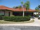 The building's exterior boasts a red tile roof, dark window frames, trimmed hedges, and a lush, green palm tree at 5785 Gardens Dr, Sarasota, FL 34243