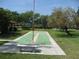 Exterior view of a community shuffleboard court surrounded by mature landscaping and a bench for relaxing at 5785 Gardens Dr, Sarasota, FL 34243