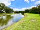 Scenic pond view with a fountain, green lawns, and mature trees under a blue sky at 8834 Whispering Oaks Trl, New Port Richey, FL 34654