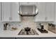 Close-up of a kitchen cooktop with white cabinets, a decorative backsplash, and stainless steel hood for a sleek look at 10399 Boyette Brook St, Riverview, FL 33569