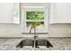 Close-up of the modern kitchen sink with granite countertops, white cabinets, and a window overlooking the backyard at 16138 Manorwood Cir, Tampa, FL 33624