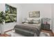 This neutral bedroom has a large window overlooking a mature tree and a plush bed with a decorative bedside table at 211 Arlington E Ave, Oldsmar, FL 34677
