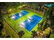 Aerial view of tennis courts at night, featuring vibrant green and blue surfaces with court lighting at 31646 Baymont Loop, Wesley Chapel, FL 33543