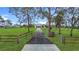 Long paved driveway leading to a charming home, framed by green lawns and a rustic wooden fence on either side at 28410 Wildlife Ln, Brooksville, FL 34602