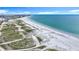 An aerial view captures a pristine white sandy beach, stretching along the serene turquoise ocean water with grassy dunes at 760 Capri Blvd, Treasure Island, FL 33706