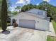 Two-car garage with gray door, exterior wall extension and landscaped yard with a beautiful, mature cypress tree at 15722 Gardenside Ln, Tampa, FL 33624