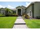 Charming green home with a lush front lawn, vibrant landscaping, and a welcoming brick walkway at 916 Bunker View Dr, Apollo Beach, FL 33572