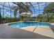 Sparkling pool area with blue water, a screened enclosure, an umbrella, and view of the greenery beyond at 12713 Grand Traverse Dr, Dade City, FL 33525