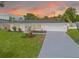 Charming home featuring a manicured front lawn, landscaping, and two-car garage against a beautiful sunset backdrop at 1723 Cypress Ave, Belleair, FL 33756