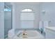 Bright bathroom featuring a soaking tub with tile surround, a glass-enclosed shower, and an arched window at 17302 Stetson Ln, Odessa, FL 33556