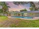 Home's backyard with a pool, green grass and some tropical foliage at sunset at 3225 Rosery Ne Rd, Largo, FL 33771