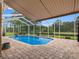 A luxurious in-ground swimming pool under a screened enclosure, surrounded by brick pavers and lush greenery at 12439 Bristol Commons Cir, Tampa, FL 33626