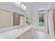 Bright bathroom featuring marble countertops, tile shower, and a door leading to the outdoor pool area at 1553 Canopy Oaks Blvd, Palm Harbor, FL 34683