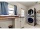 Laundry room features stacked washer and dryer, counter space, cabinets, and a window with blue curtains at 1868 Lombardy Dr, Clearwater, FL 33755