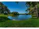 Picturesque view of a serene pond surrounded by manicured grass and lush trees on a clear day at 2690 Coral Landings Blvd # 122, Palm Harbor, FL 34684