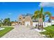 Elegant two-story home with a large circular paver driveway, lush landscaping, and mature trees on a sunny day at 311 22Nd St, Belleair Beach, FL 33786