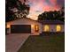 This is an eye-level view of a single-story home with a gray garage door and arched front windows at sunset at 6204 Walsh Ln, Tampa, FL 33625