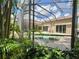 View of the backyard's pool area through tropical landscaping and the enclosing screen at 10675 Park Place Dr, Largo, FL 33778