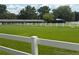 Beautiful horse farm with green grass, white fence, stalls, and riding area on a sunny day at 22422 Stillwood Dr, Land O Lakes, FL 34639